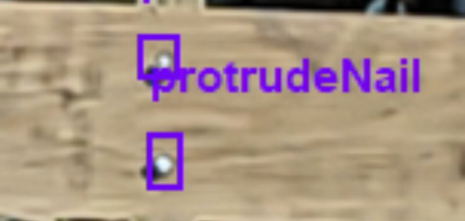 Close-up camera frame of a deck board with two nail heads standing proud of the surface, each boxed and labelled as a protruding nail by the system